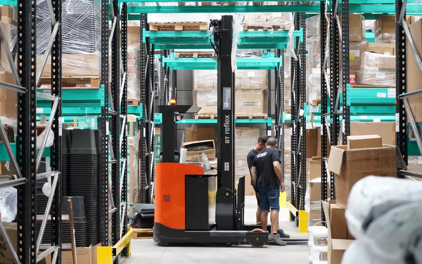 A warehouse aisle with a forklift, workers and racked pallets, the frame a vision model is watching